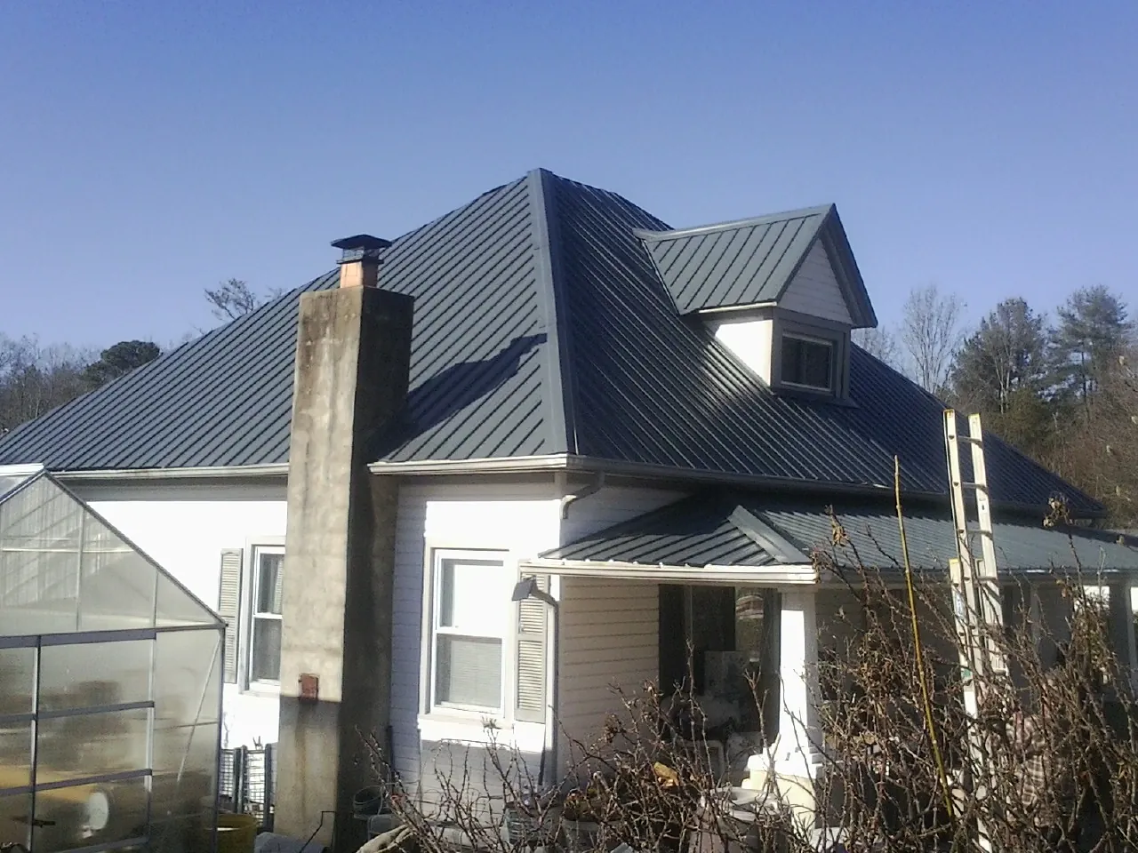 Dark blue standing seam metal roof on a white farmhouse with dormer — Slate & Tile Roof Repair by Roofing Brothers in Street