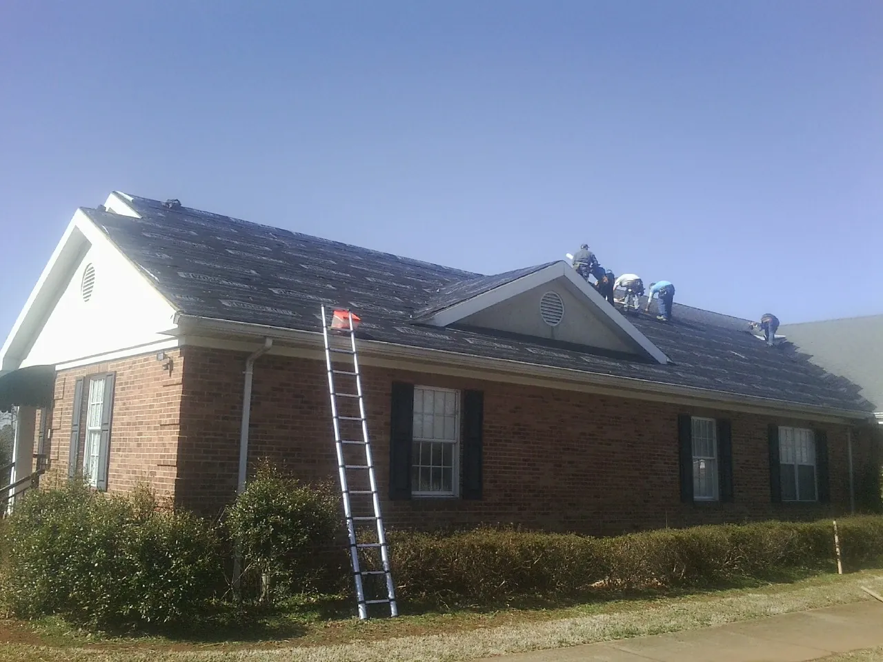 Crew tearing shingles off a brick ranch roof with a ladder set — Metal Roof Repair work by our crew in Street