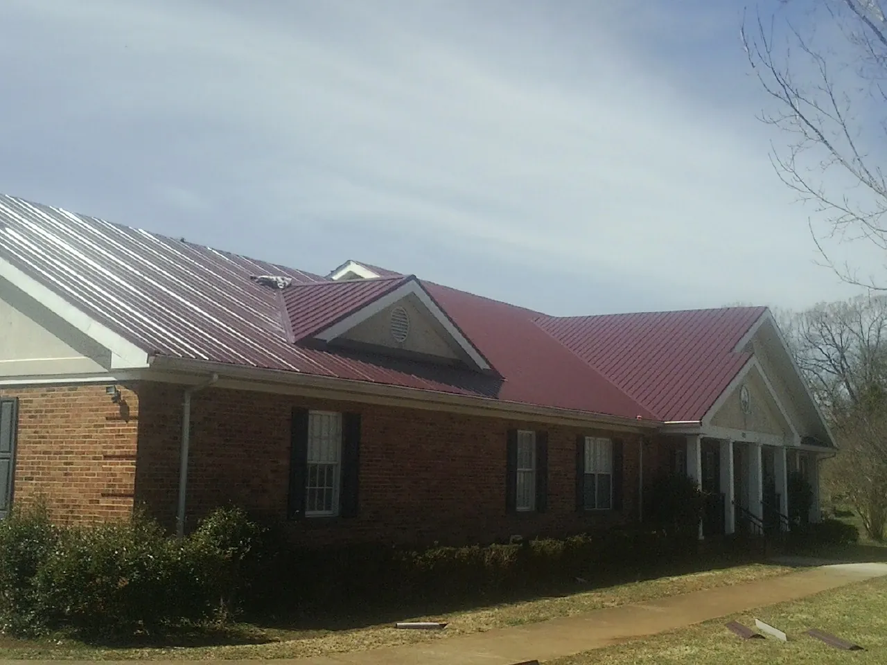 Red metal roof with gabled entries on a long brick building, from a Hail Damage Roof Repair job in Street