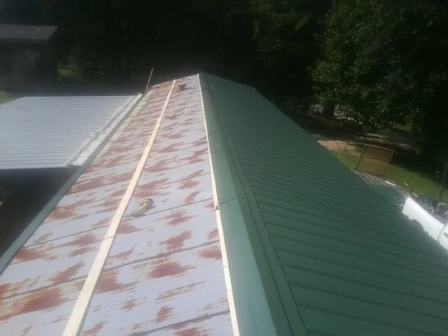 Old rusted panels beside newly installed green metal roofing — Wind Damage Roof Repair by Roofing Brothers in Street