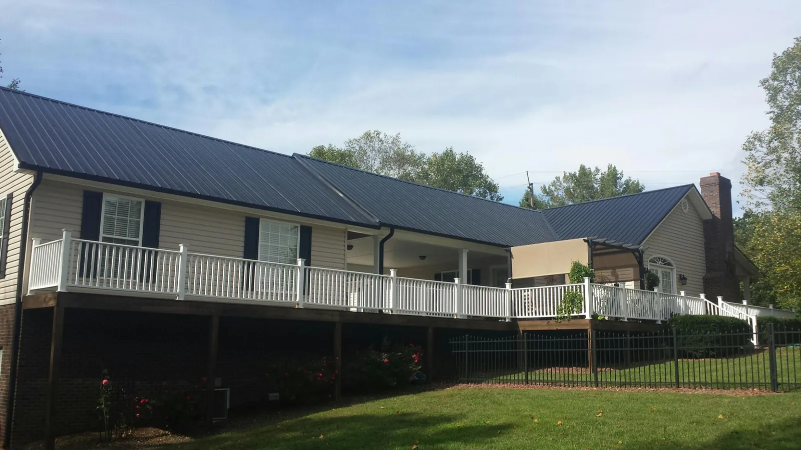 Black metal roof above a long white railed deck on a hillside home in Street