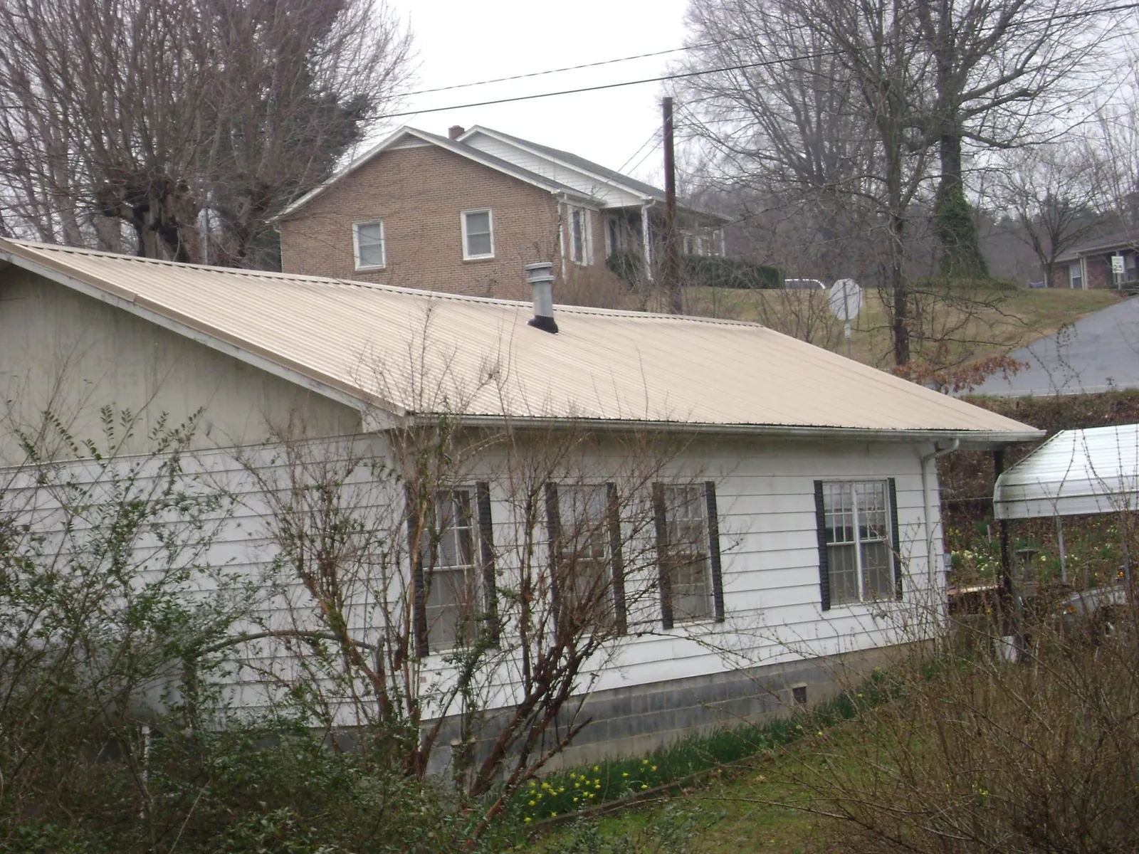 Tan metal roof on a white sided house set into a hillside — Commercial Roofing by Roofing Brothers in Street