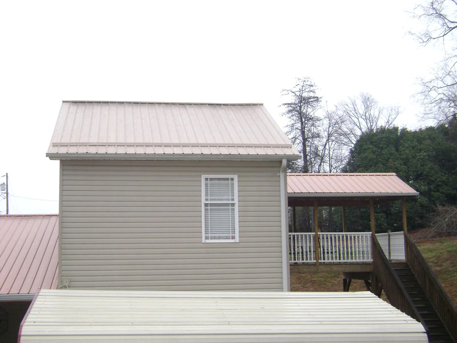 Tan metal roofs on a two story addition and attached porch, from a Roof Replacement job in Street